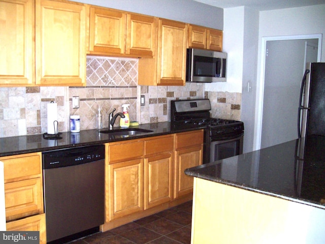 kitchen with backsplash, appliances with stainless steel finishes, dark tile patterned floors, dark stone countertops, and sink