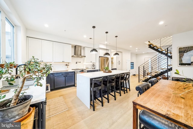 kitchen with pendant lighting, wall chimney range hood, a breakfast bar, stainless steel appliances, and blue cabinets