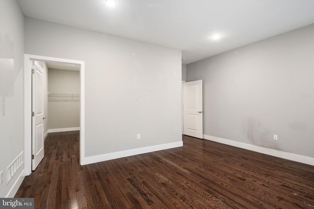 unfurnished bedroom featuring dark wood-type flooring, a walk in closet, and a closet