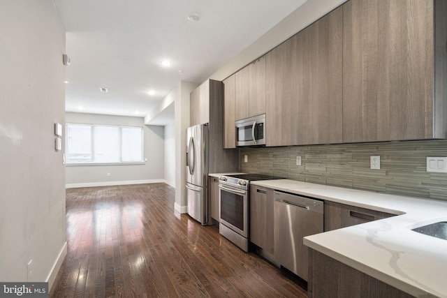 kitchen featuring light stone counters, appliances with stainless steel finishes, dark wood-type flooring, and decorative backsplash