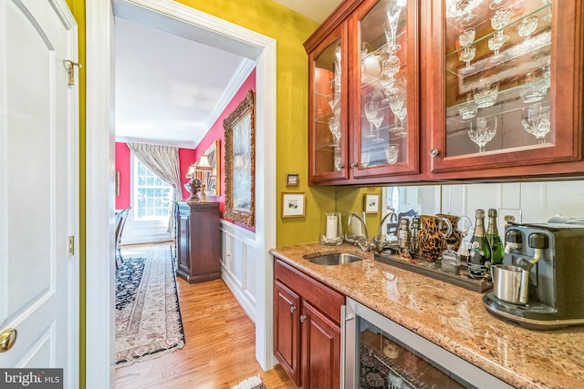 bar with light stone countertops, sink, light wood-type flooring, wine cooler, and ornamental molding