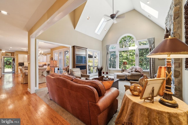 living room featuring a wealth of natural light, high vaulted ceiling, ceiling fan with notable chandelier, and light hardwood / wood-style floors