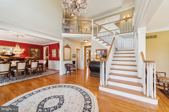 foyer entrance with a towering ceiling, ornate columns, crown molding, hardwood / wood-style flooring, and a chandelier