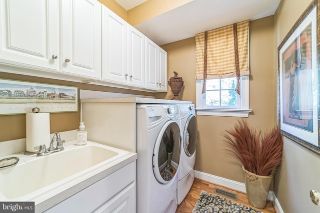 clothes washing area featuring light hardwood / wood-style flooring, washer and dryer, cabinets, and sink