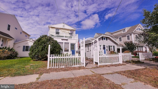 view of front of property featuring a front yard, a balcony, and a fenced front yard
