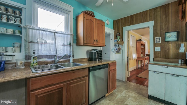 kitchen with light wood-type flooring, sink, wood walls, ceiling fan, and stainless steel dishwasher