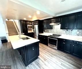 kitchen featuring an island with sink, decorative backsplash, stainless steel appliances, sink, and light hardwood / wood-style floors