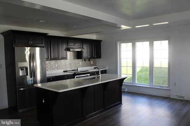 kitchen with dark hardwood / wood-style floors, sink, backsplash, appliances with stainless steel finishes, and an island with sink