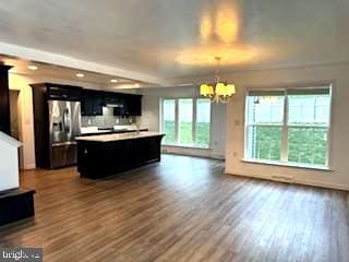 kitchen featuring stainless steel fridge, a kitchen island, decorative light fixtures, a notable chandelier, and dark hardwood / wood-style floors