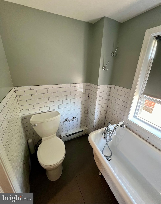 bathroom with tile patterned floors, a tub to relax in, toilet, a baseboard radiator, and tile walls