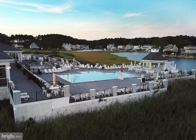 pool at dusk with a lawn, a water view, and a patio area