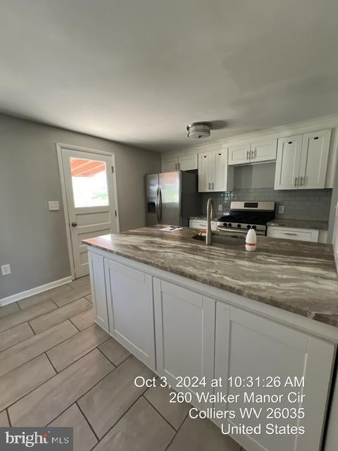 kitchen with dark stone counters, stainless steel appliances, white cabinets, and decorative backsplash