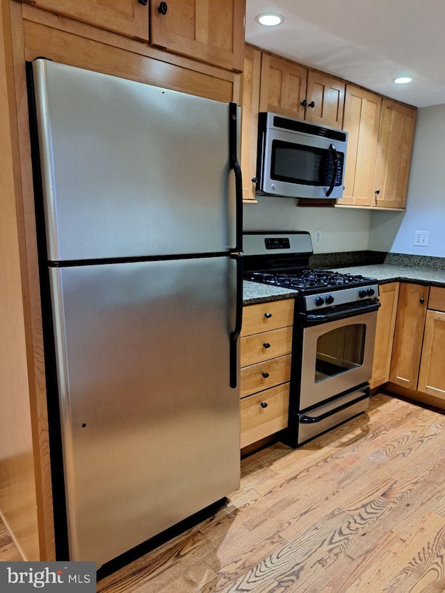 kitchen featuring appliances with stainless steel finishes, light wood-type flooring, and dark stone counters