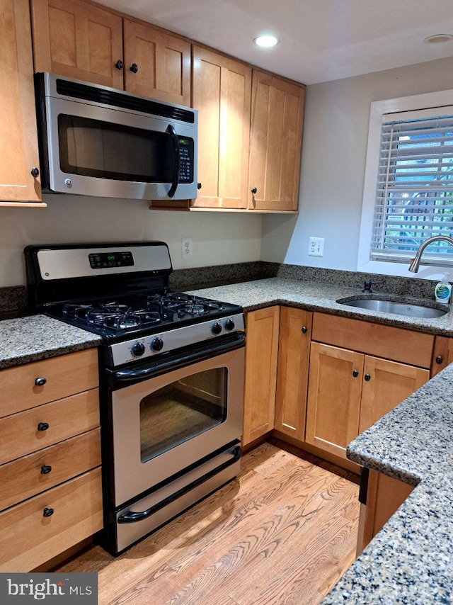 kitchen with light stone countertops, stainless steel appliances, light hardwood / wood-style floors, and sink