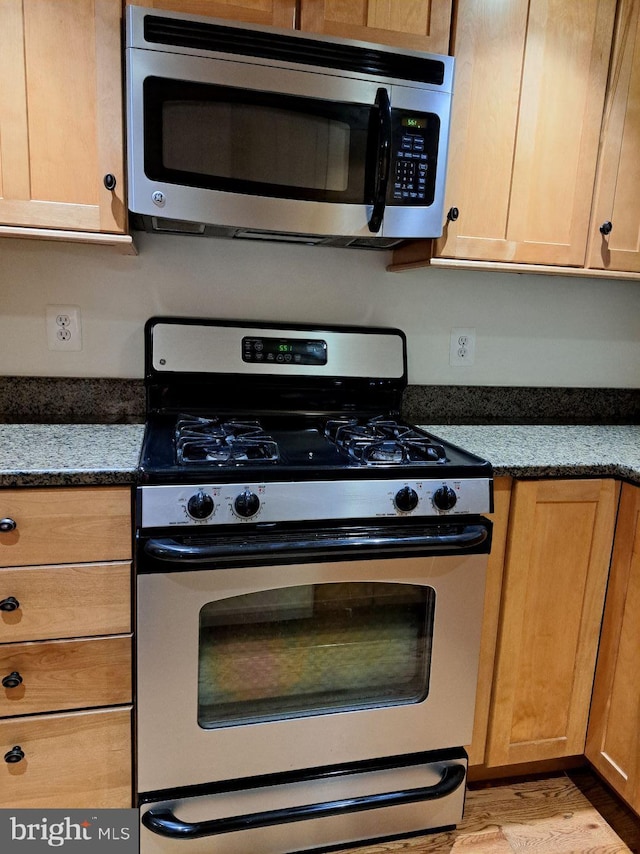 kitchen featuring stainless steel appliances, light wood-type flooring, and dark stone counters