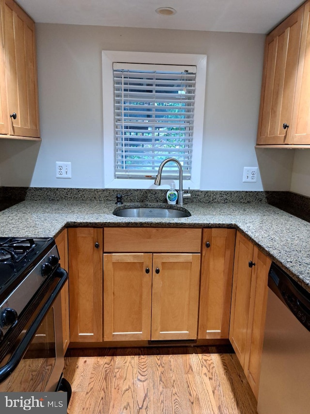 kitchen featuring black gas stove, dishwasher, light hardwood / wood-style floors, light stone counters, and sink