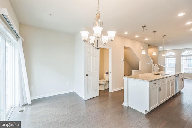 kitchen featuring light stone counters, hanging light fixtures, sink, a center island with sink, and dark hardwood / wood-style floors