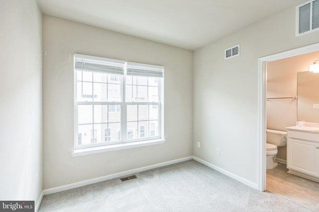 unfurnished bedroom featuring connected bathroom and light carpet