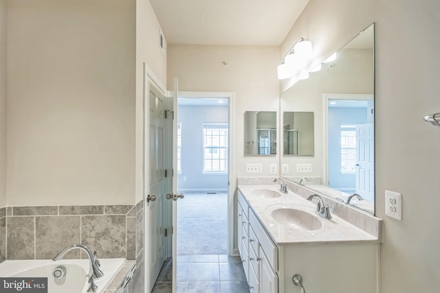 bathroom with tiled tub, vanity, tile patterned flooring, and a wealth of natural light