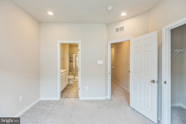 unfurnished bedroom with light colored carpet, a closet, connected bathroom, and a spacious closet