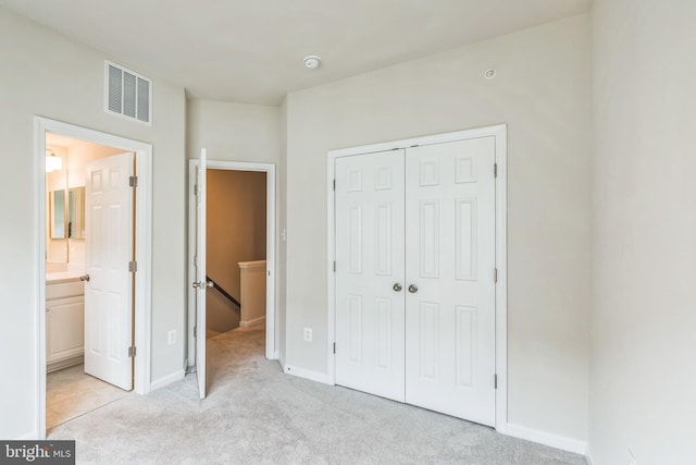 unfurnished bedroom featuring light carpet, a closet, and ensuite bathroom