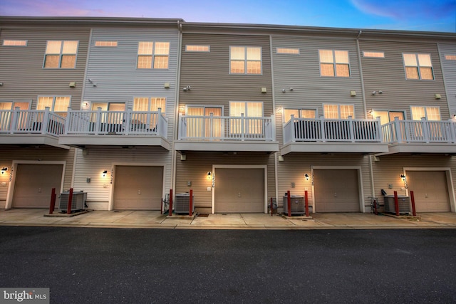 back house at dusk featuring a balcony, a garage, and central AC