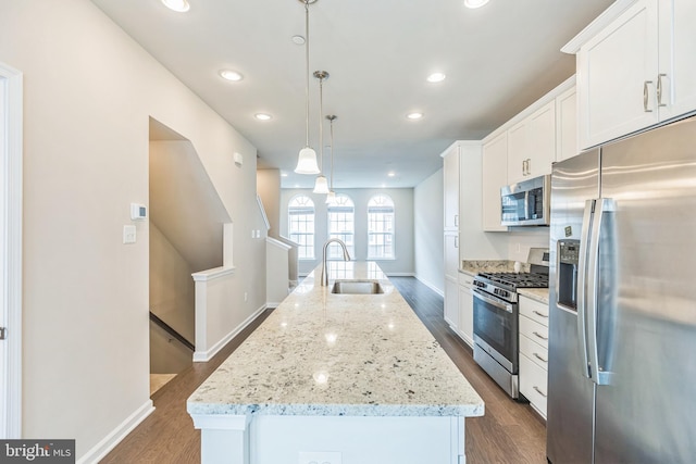 kitchen featuring an island with sink, white cabinetry, appliances with stainless steel finishes, and decorative light fixtures