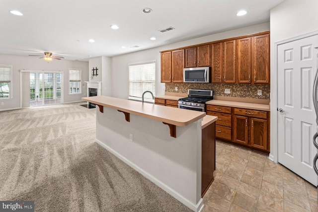 kitchen featuring ceiling fan, backsplash, stainless steel appliances, a kitchen breakfast bar, and light colored carpet