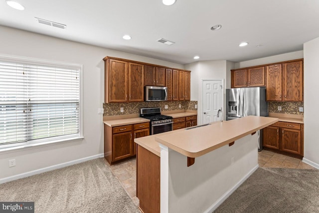 kitchen featuring sink, an island with sink, a kitchen breakfast bar, stainless steel appliances, and decorative backsplash