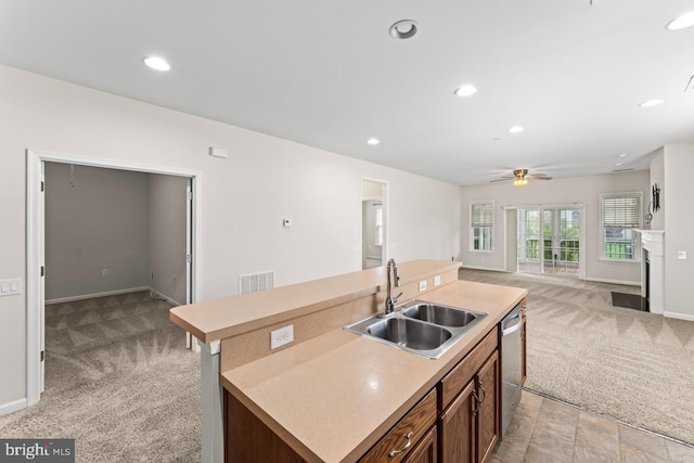 kitchen with an island with sink, ceiling fan, stainless steel dishwasher, sink, and light carpet