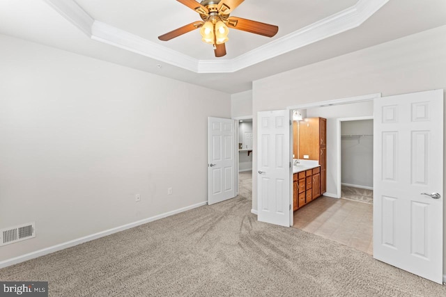 unfurnished bedroom with a raised ceiling, ceiling fan, light colored carpet, and a closet