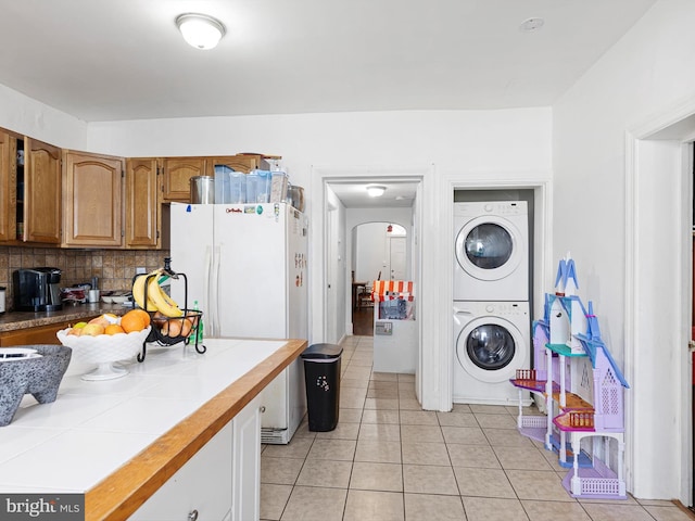 kitchen featuring tile countertops, light tile patterned floors, stacked washer / dryer, white fridge, and tasteful backsplash