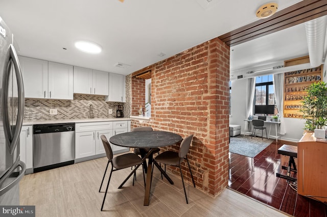 kitchen featuring appliances with stainless steel finishes, white cabinetry, backsplash, light wood-type flooring, and sink