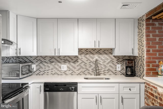 kitchen with dishwasher, sink, white cabinetry, decorative backsplash, and brick wall