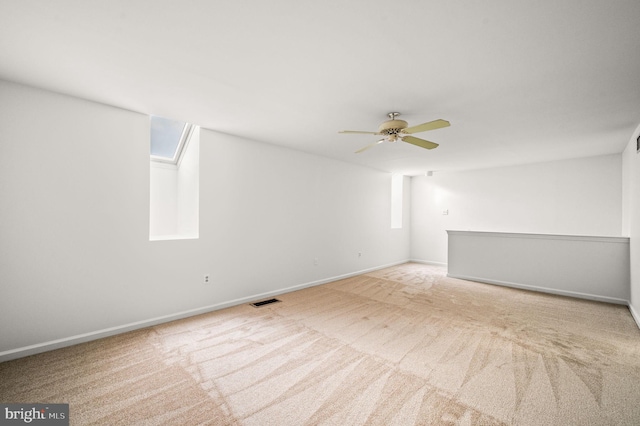 carpeted spare room with ceiling fan, a skylight, and a wealth of natural light