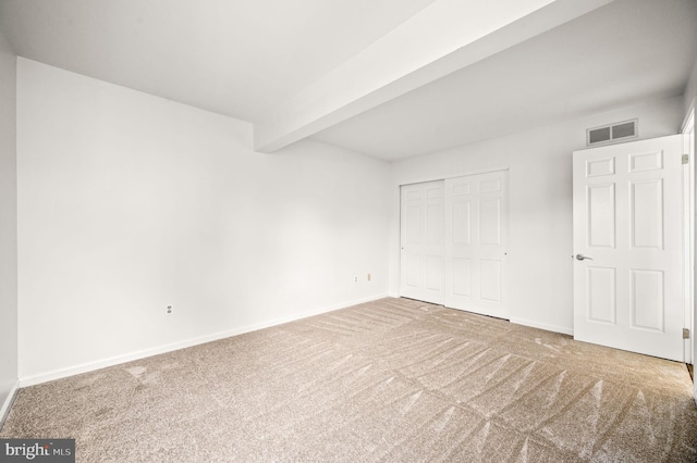 unfurnished bedroom featuring carpet floors, beamed ceiling, and a closet