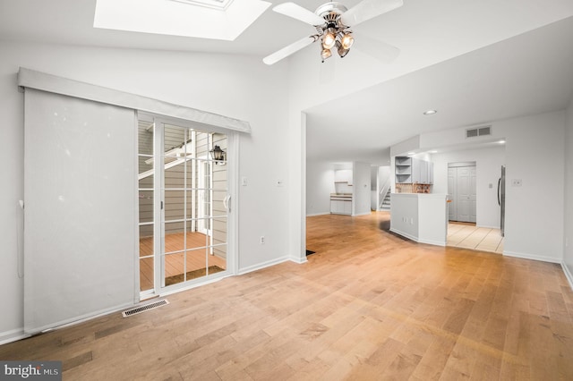 unfurnished living room with ceiling fan, lofted ceiling with skylight, and light hardwood / wood-style floors