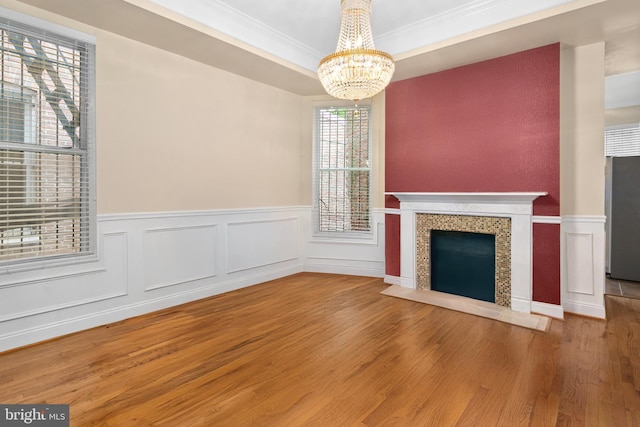 unfurnished living room featuring hardwood / wood-style flooring, a tiled fireplace, crown molding, and a chandelier