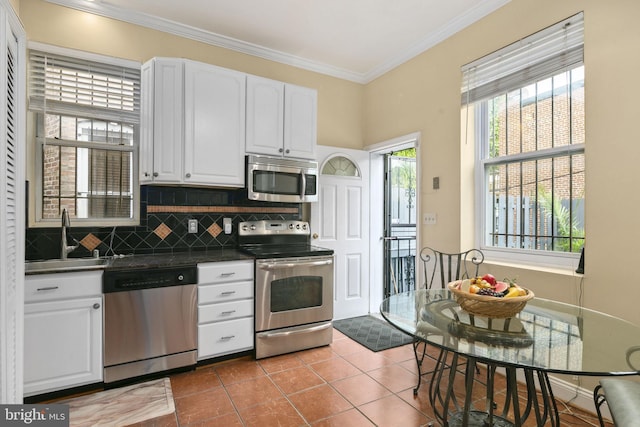 kitchen with appliances with stainless steel finishes, ornamental molding, sink, tile patterned flooring, and white cabinetry