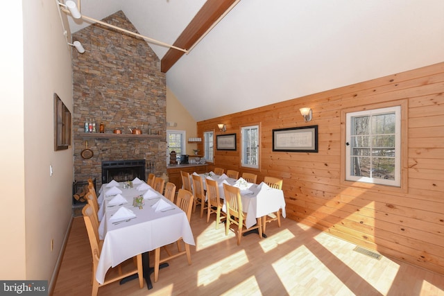 dining room with high vaulted ceiling, wooden walls, hardwood / wood-style floors, and a stone fireplace