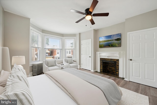 bedroom with dark hardwood / wood-style flooring, radiator, ceiling fan, and a fireplace