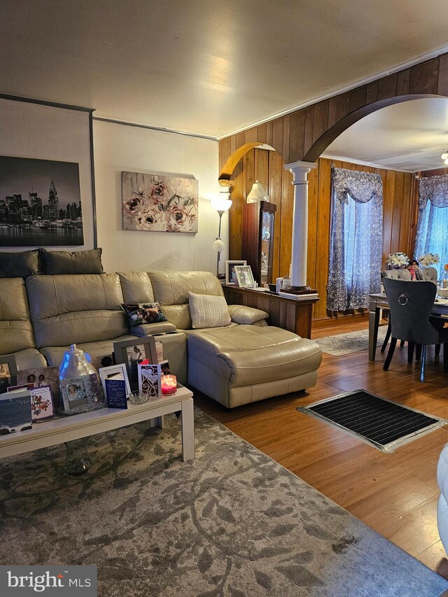 living room featuring wooden walls, hardwood / wood-style floors, ornate columns, and crown molding