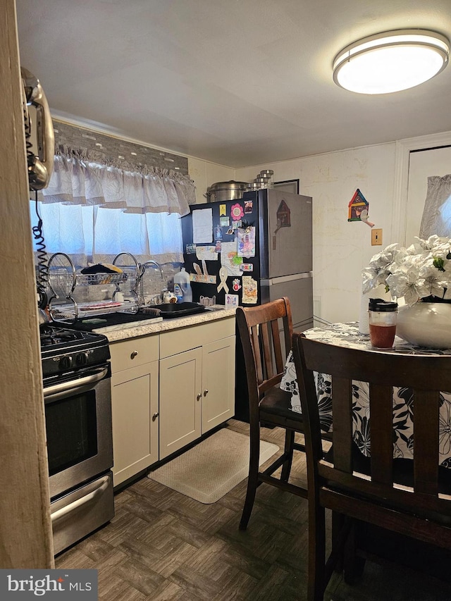 kitchen with white cabinetry, dark parquet floors, stainless steel range with gas stovetop, refrigerator, and sink