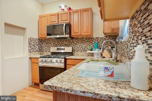 kitchen featuring light hardwood / wood-style floors, sink, light stone countertops, backsplash, and appliances with stainless steel finishes