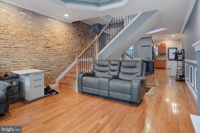 living room with brick wall, light wood-type flooring, and ornamental molding