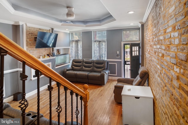 living room featuring light hardwood / wood-style floors, ceiling fan, crown molding, a tray ceiling, and brick wall