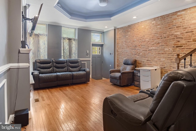 living room featuring brick wall, a tray ceiling, crown molding, and light hardwood / wood-style floors