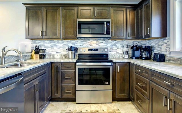 kitchen with dark brown cabinets, stainless steel appliances, light stone counters, and sink