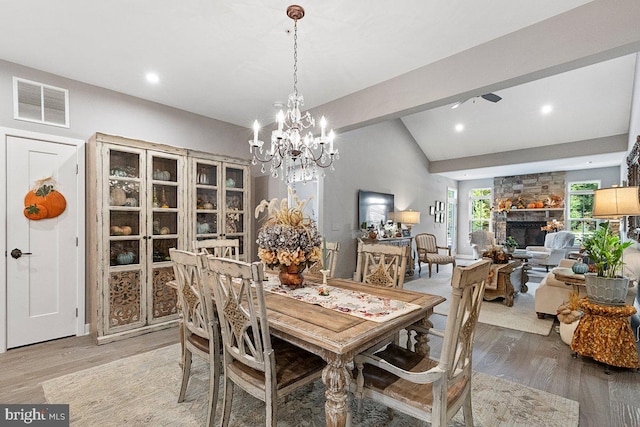 dining room with an inviting chandelier, a fireplace, lofted ceiling with beams, and hardwood / wood-style floors