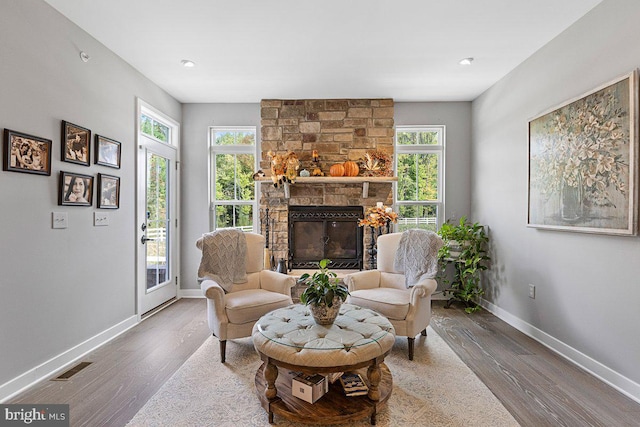 living room with hardwood / wood-style flooring, a healthy amount of sunlight, and a stone fireplace